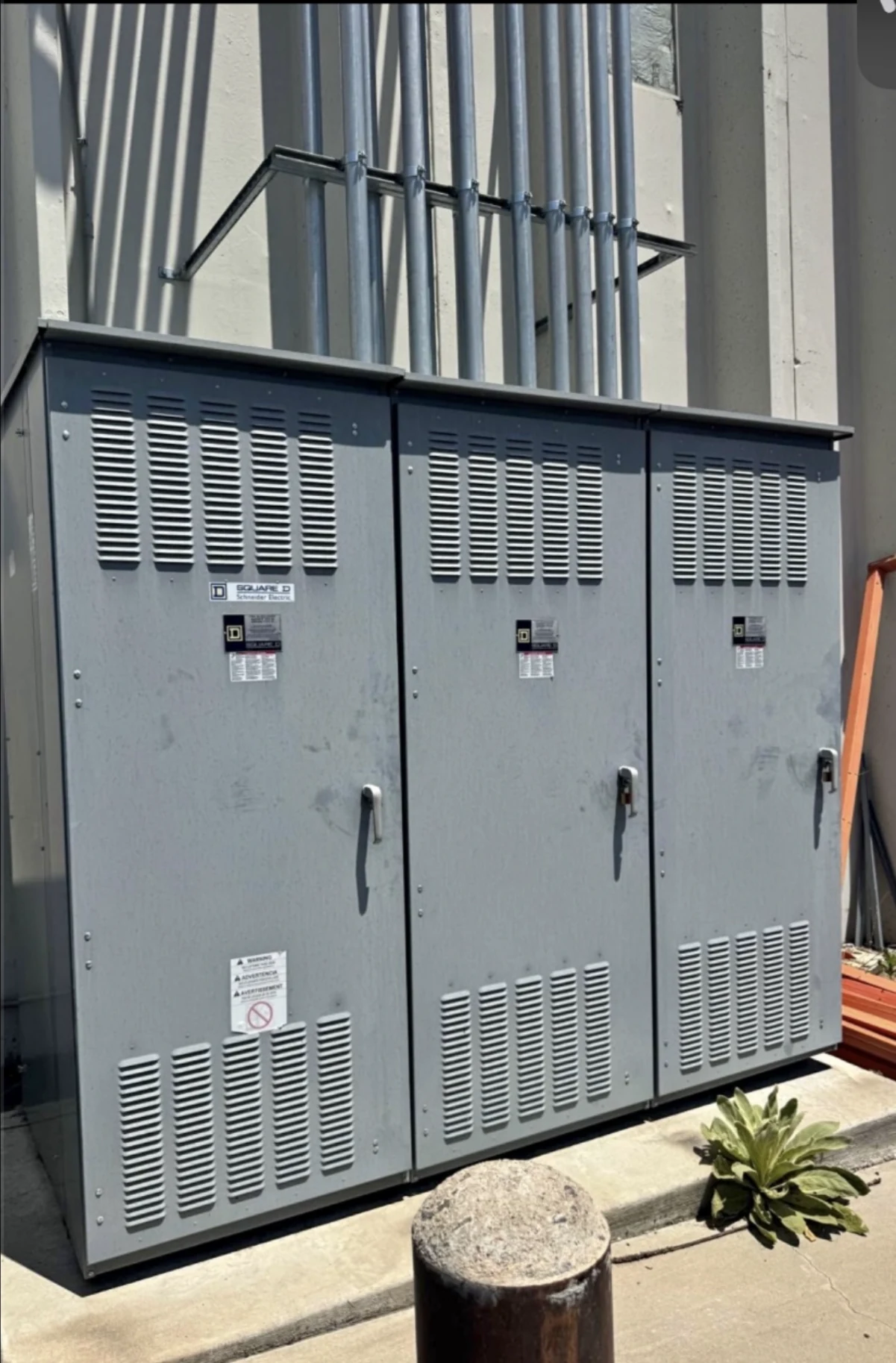 Outdoor electrical switchgear lineup with three gray enclosures on a concrete pad.