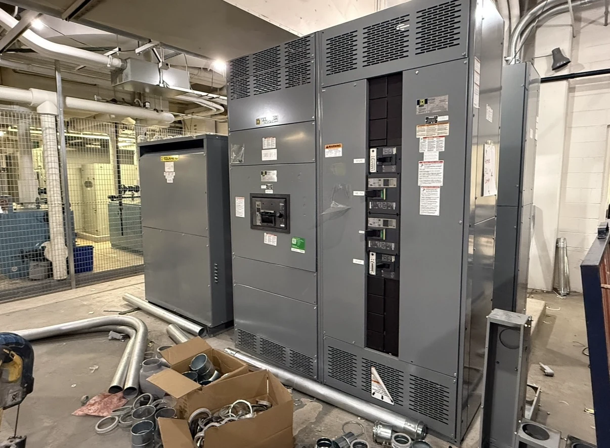 Gray switchgear lineup and transformer installed in an electrical room.