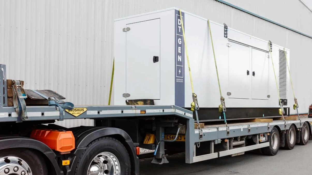 Large white industrial generator secured on a flatbed transport trailer.