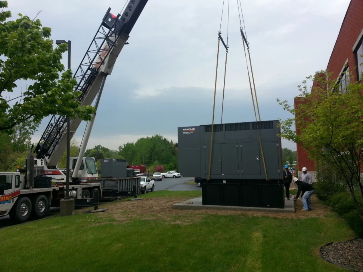 Industrial generator being lifted by crane onto a concrete equipment pad.