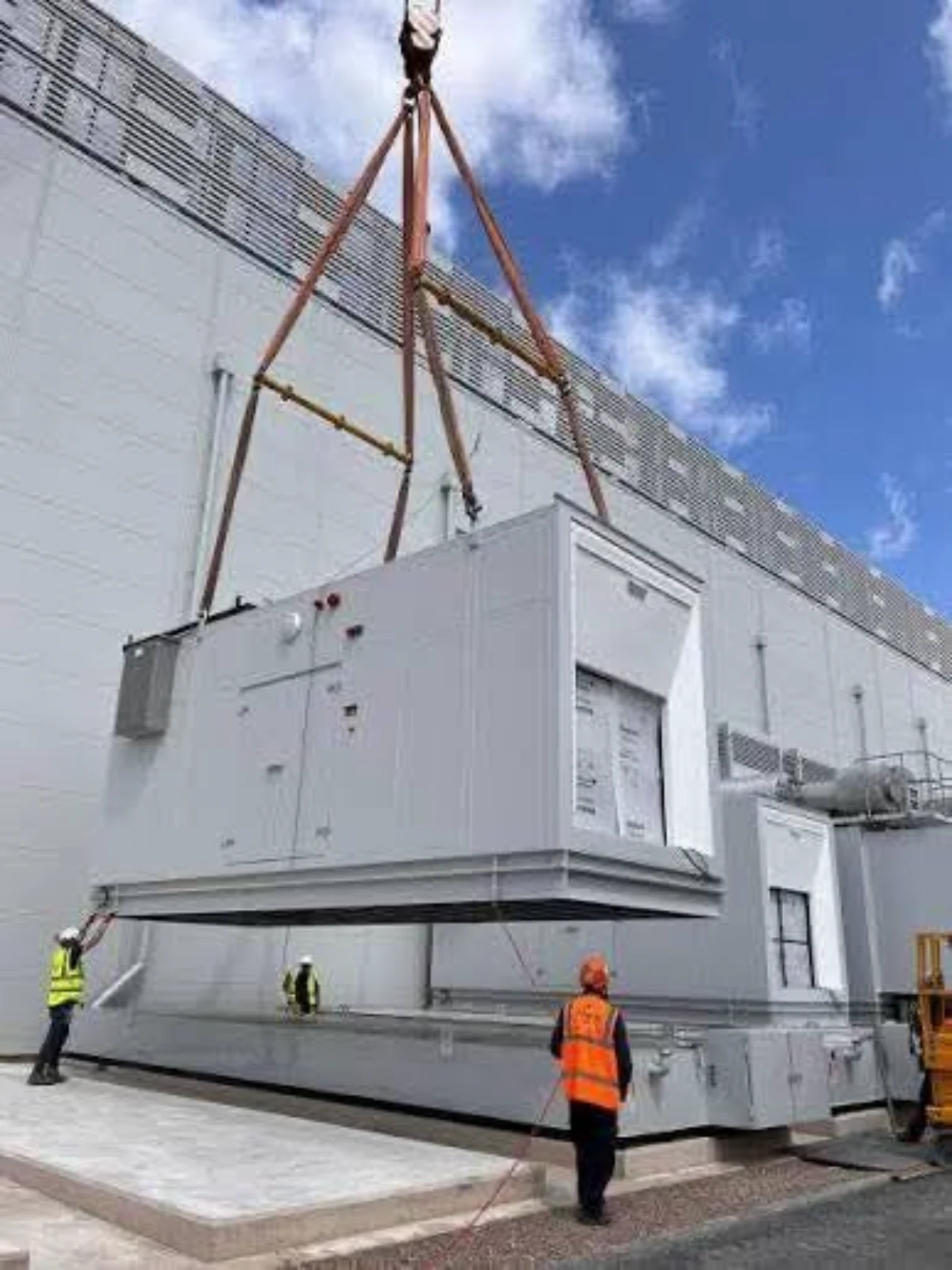 Large electrical equipment enclosure being lifted by crane as workers guide it.
