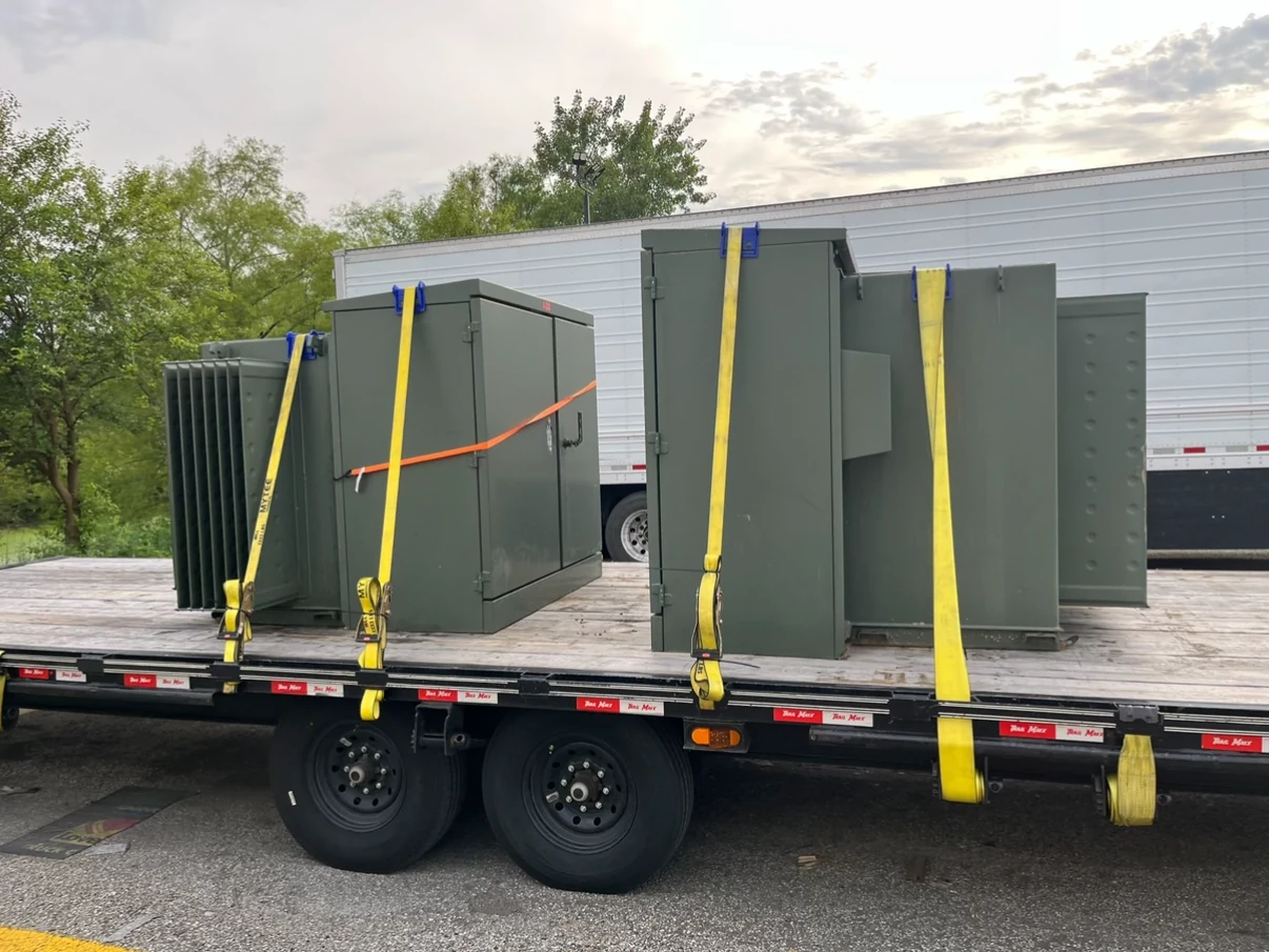 Two green padmount transformers strapped to a flatbed trailer.