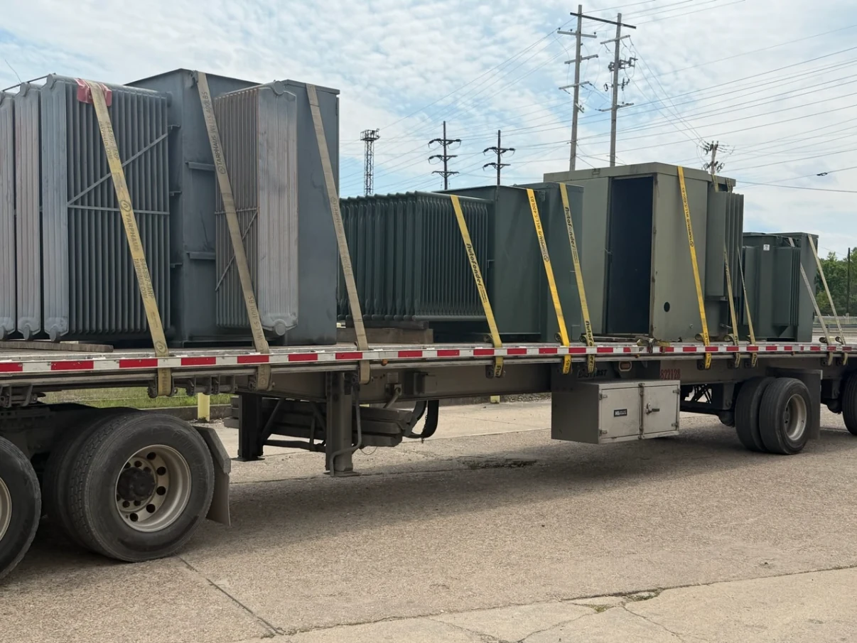 Several large electrical transformers secured to a flatbed truck trailer.