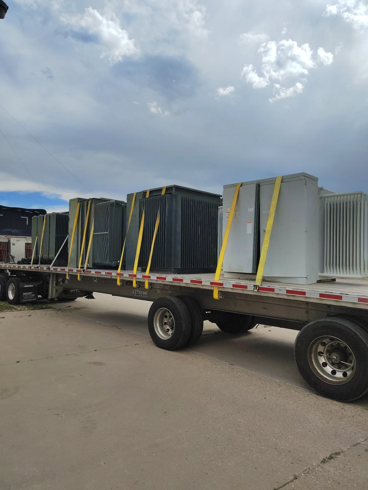 Multiple transformers strapped to a flatbed beneath a cloudy sky.