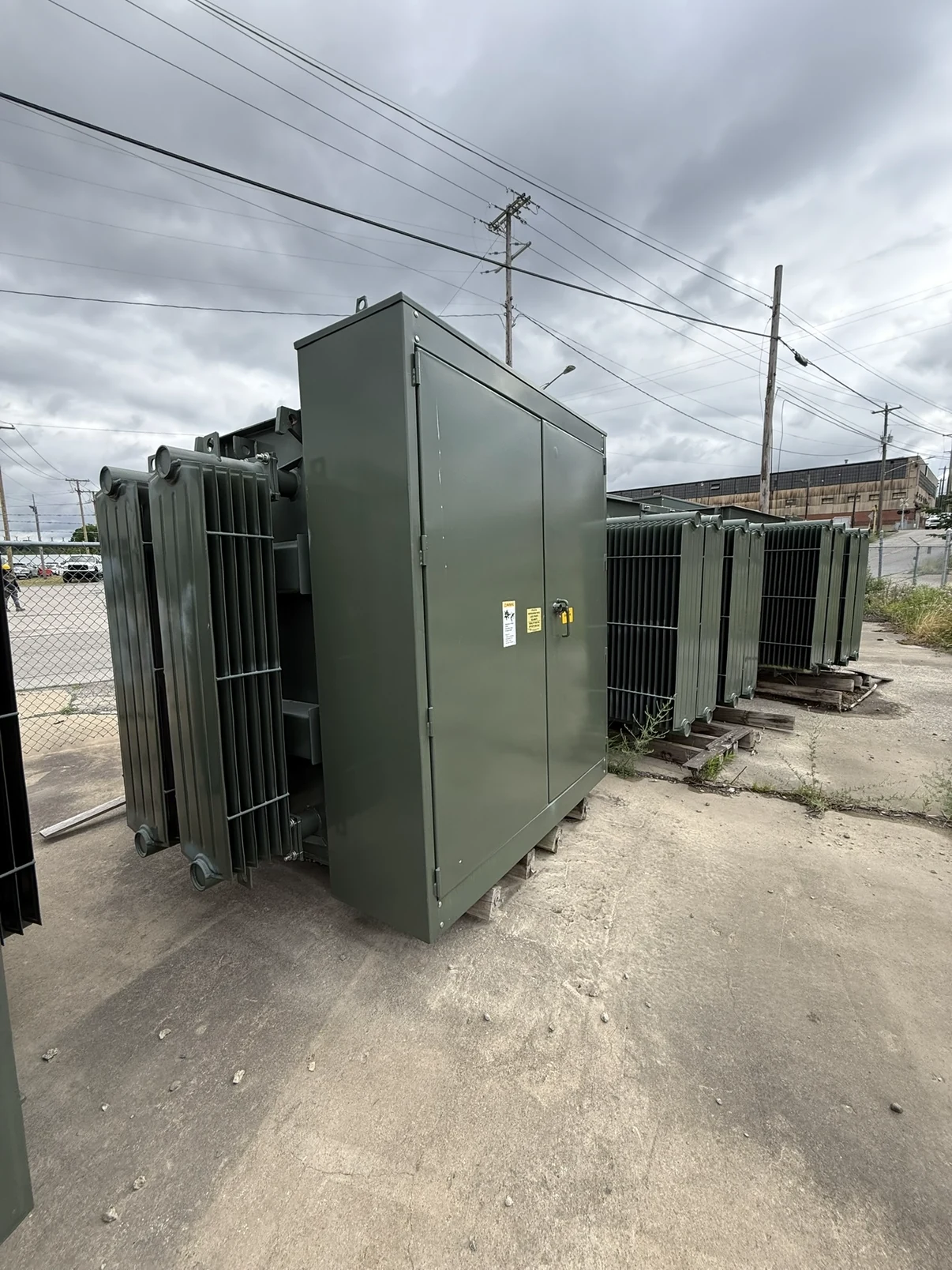 Row of green pad-mounted electrical transformers in an outdoor equipment yard.