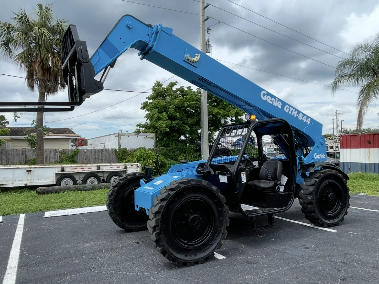 Blue telehandler with fork attachment and partially raised boom.
