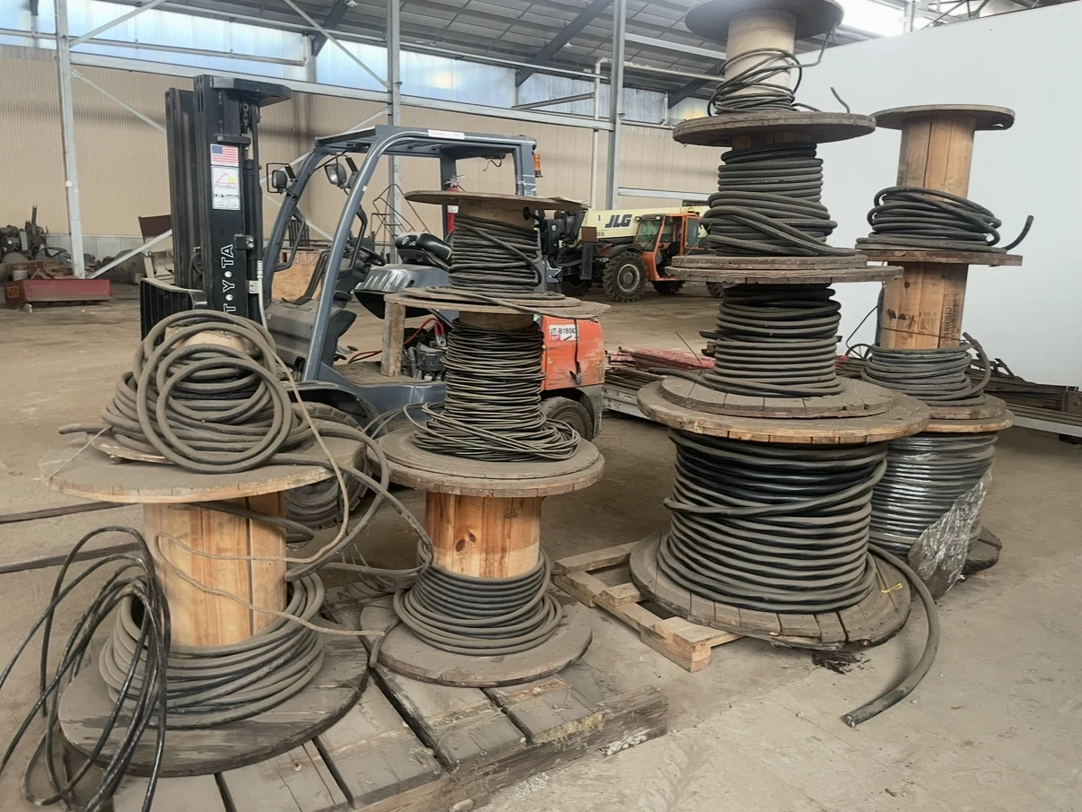 Wooden spools of thick electrical cable stacked in a warehouse.